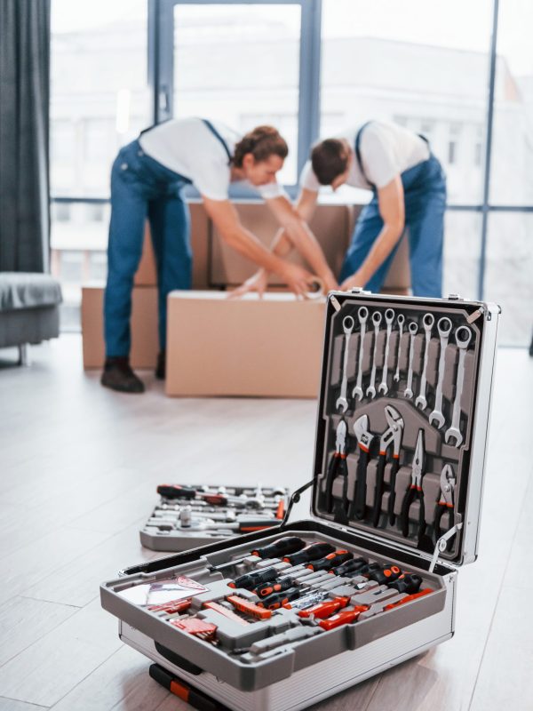 Case with equipment. Two young movers in blue uniform working indoors in the room